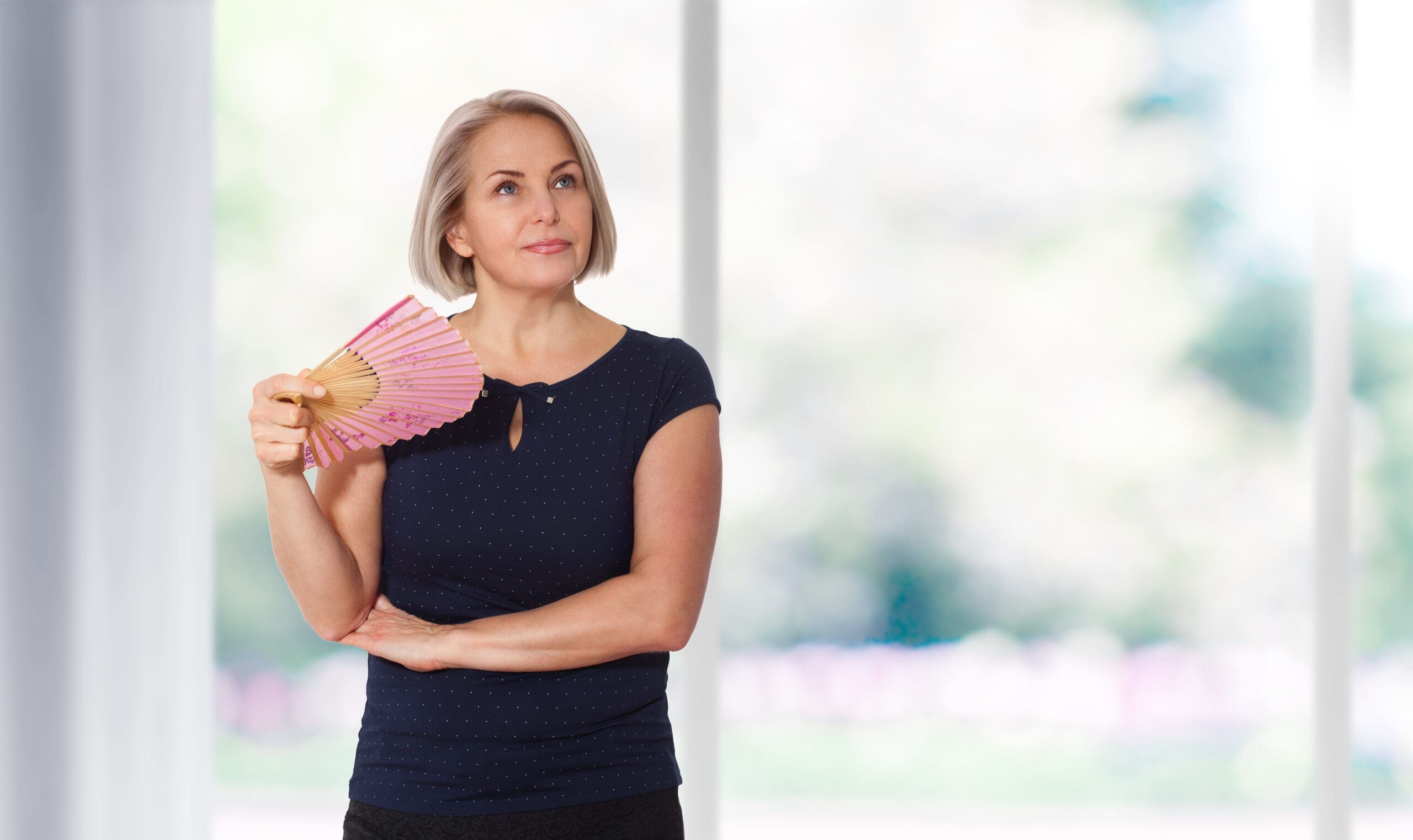 Attractive middle aged woman relaxing with fan. Mature woman experiencing hot flush from menopause Menopause symptoms