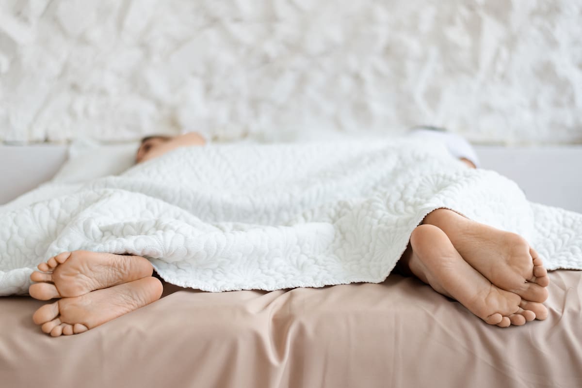 Sexual problems. Husband and wife lying apart with their backs to each other in bed, closeup of feet, free space