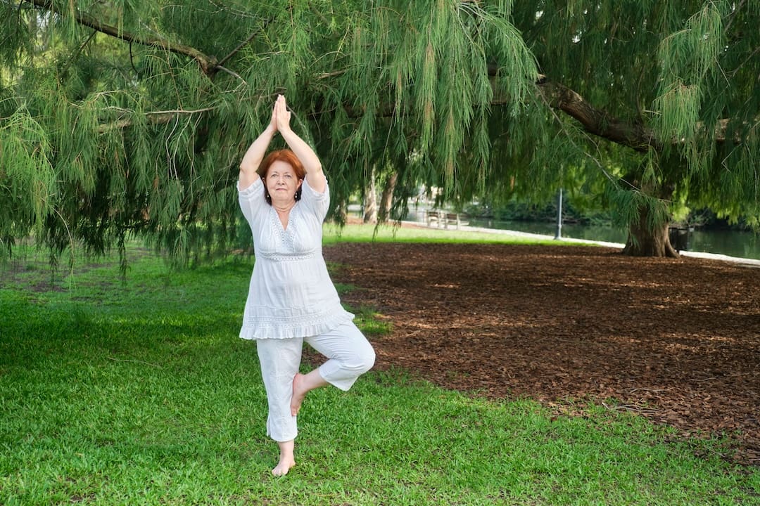 Senior Hispanic woman practicing yoga. Wellness, active and healthy lifestyle. Mature Hispanic woman in white clothes practicing standing on one leg for health.